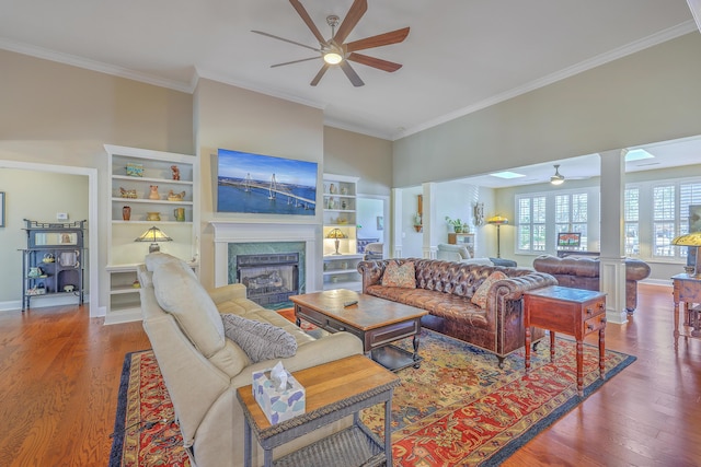 living room featuring crown molding, a glass covered fireplace, wood finished floors, and ornate columns