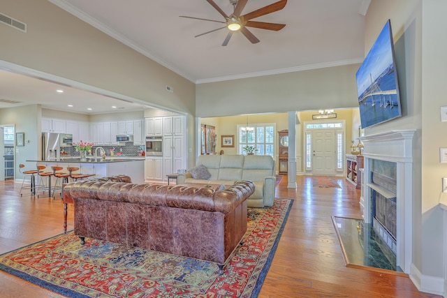 living room with baseboards, visible vents, crown molding, light wood-type flooring, and ceiling fan with notable chandelier