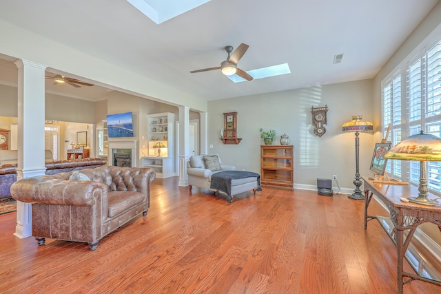 living area with a skylight, decorative columns, light wood-style flooring, and ceiling fan