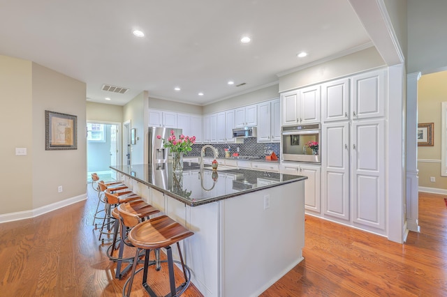 kitchen with visible vents, light wood-style flooring, stainless steel appliances, a kitchen bar, and white cabinetry