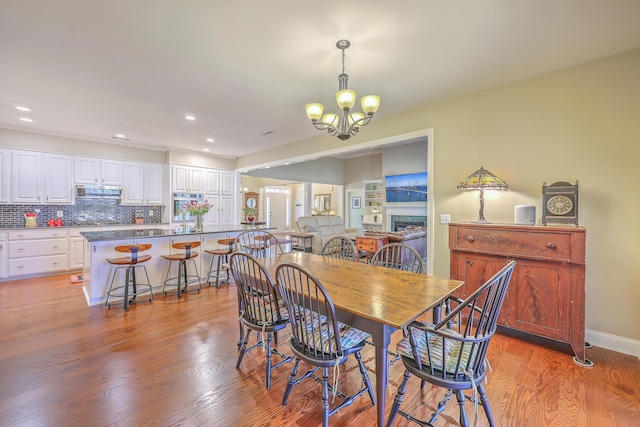 dining space with recessed lighting, a notable chandelier, a fireplace, and light wood-style flooring