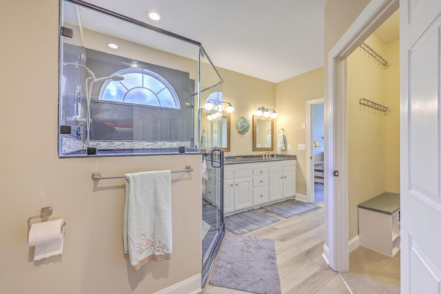 bathroom featuring a shower with shower door, a sink, wood finished floors, baseboards, and double vanity