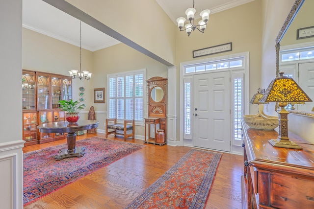 foyer entrance with baseboards, ornamental molding, wood finished floors, a high ceiling, and a notable chandelier