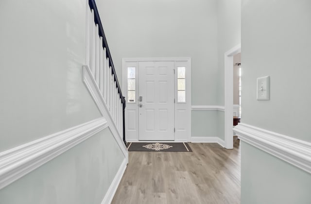 entrance foyer featuring light wood-type flooring, stairs, a towering ceiling, and baseboards