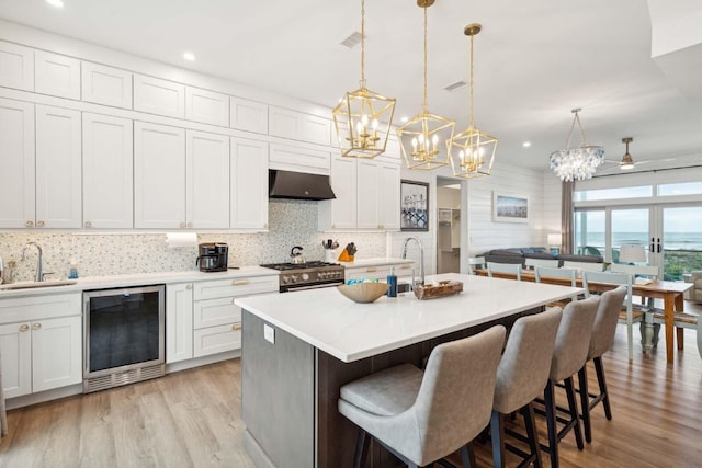 kitchen with wine cooler, a breakfast bar area, a sink, under cabinet range hood, and stainless steel gas range oven