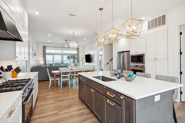 kitchen with stainless steel appliances, a sink, visible vents, open floor plan, and range hood