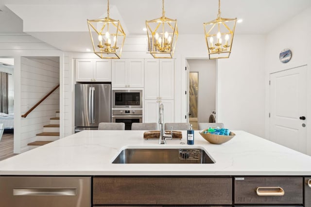 kitchen with light stone counters, pendant lighting, stainless steel appliances, a kitchen island with sink, and a sink