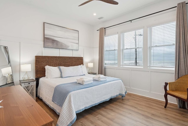 bedroom with ceiling fan, visible vents, a decorative wall, and wood finished floors