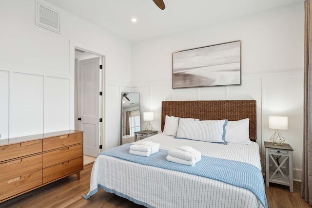 bedroom with wood finished floors, visible vents, and a decorative wall