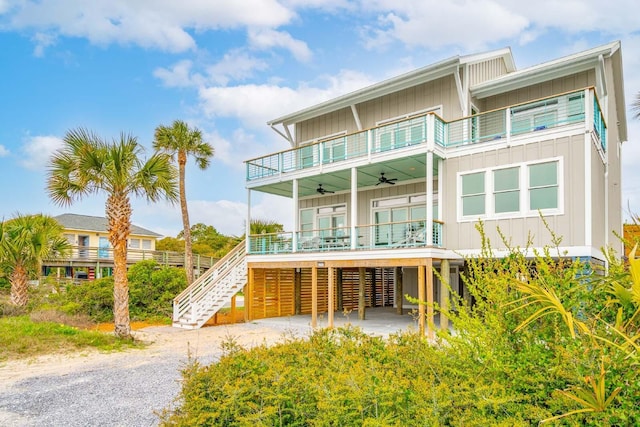 back of property with board and batten siding, ceiling fan, a balcony, and stairs