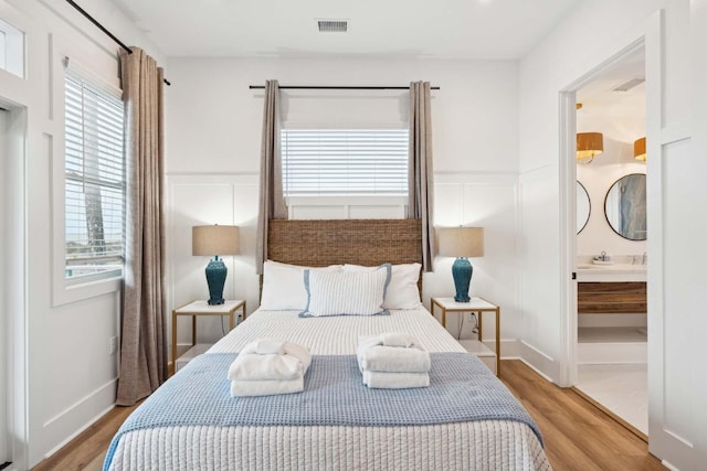 bedroom with ensuite bath, visible vents, wood finished floors, and wainscoting