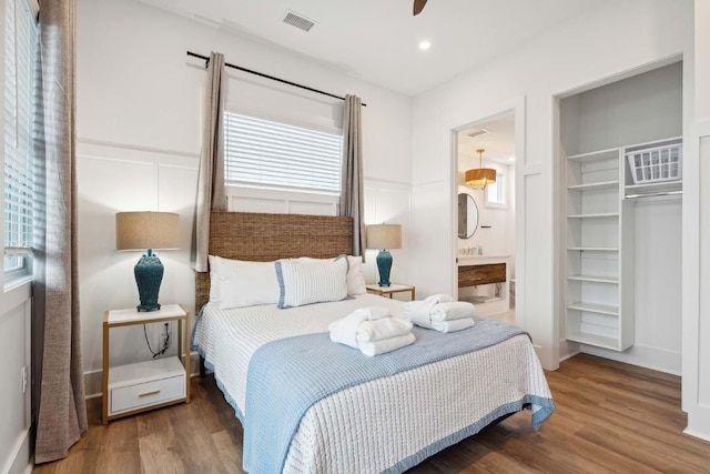 bedroom with ensuite bathroom, a spacious closet, wood finished floors, and visible vents