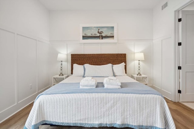 bedroom with wood finished floors, visible vents, and a decorative wall