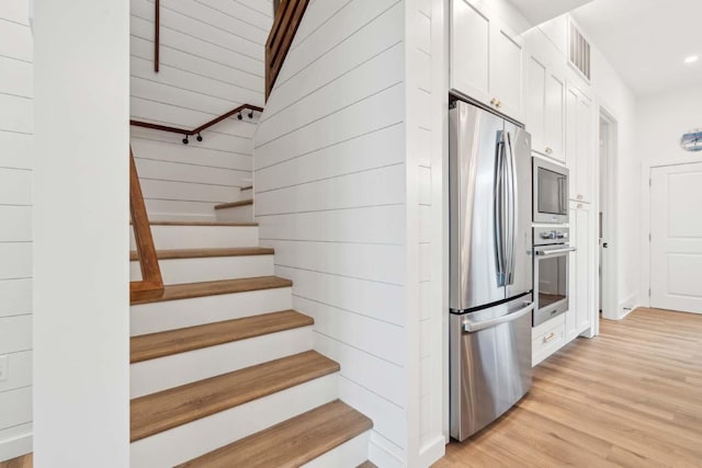 kitchen featuring stainless steel appliances, visible vents, light wood-style floors, white cabinets, and vaulted ceiling