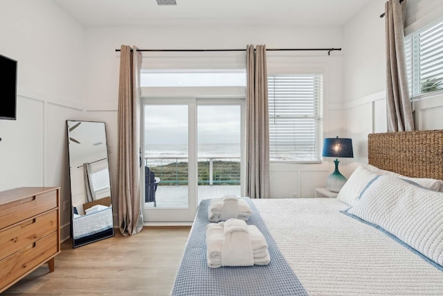 bedroom featuring light wood-type flooring, visible vents, a decorative wall, and wainscoting