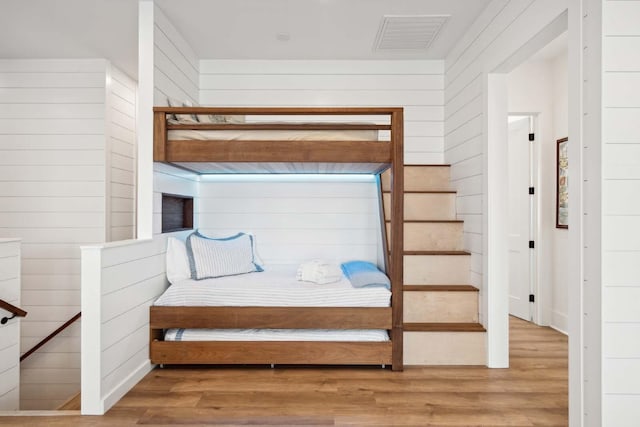 bedroom featuring wood finished floors, visible vents, and wooden walls