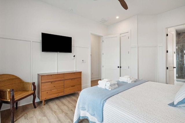 bedroom featuring light wood-style floors, wainscoting, a ceiling fan, and a decorative wall