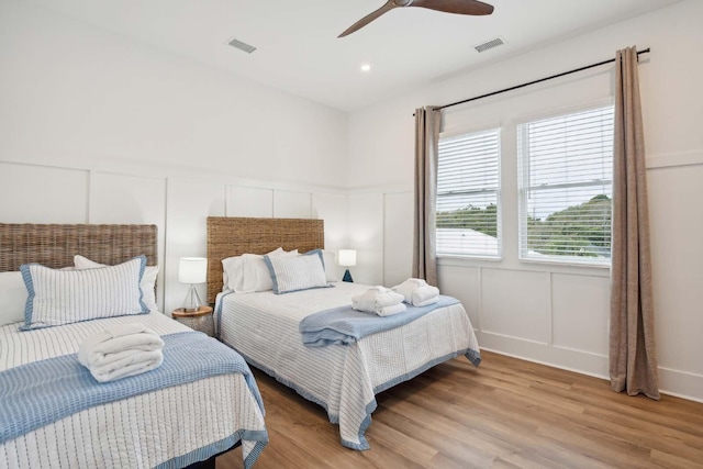 bedroom featuring visible vents, a decorative wall, light wood-style flooring, and ceiling fan