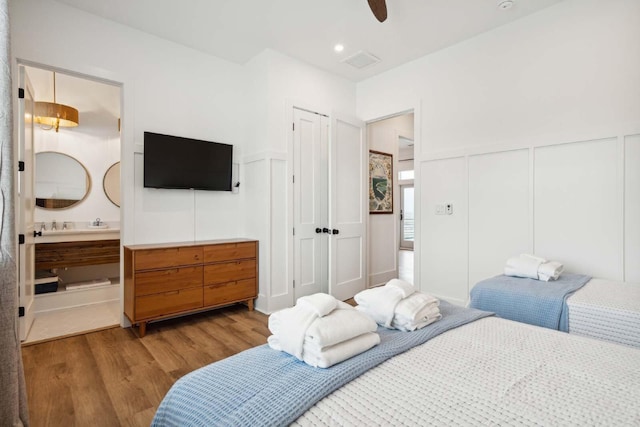 bedroom featuring a decorative wall, a wainscoted wall, wood finished floors, visible vents, and ensuite bath