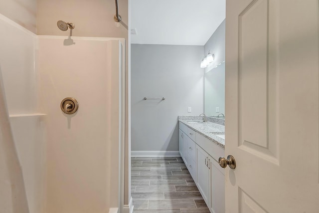 bathroom with baseboards, double vanity, walk in shower, wood tiled floor, and a sink