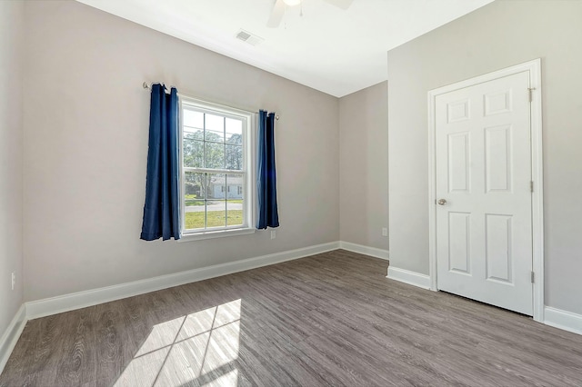 empty room featuring wood finished floors, baseboards, a ceiling fan, and visible vents