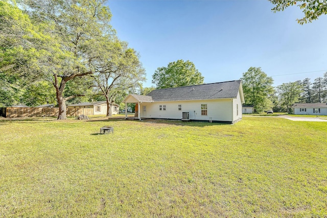 rear view of property featuring roof with shingles, central air condition unit, an outdoor fire pit, fence, and a lawn