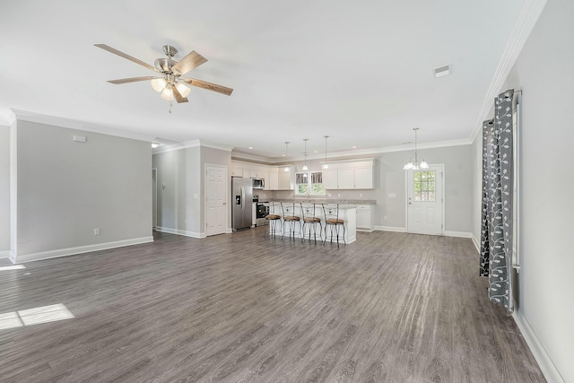 unfurnished living room with dark wood-type flooring, baseboards, crown molding, and ceiling fan with notable chandelier