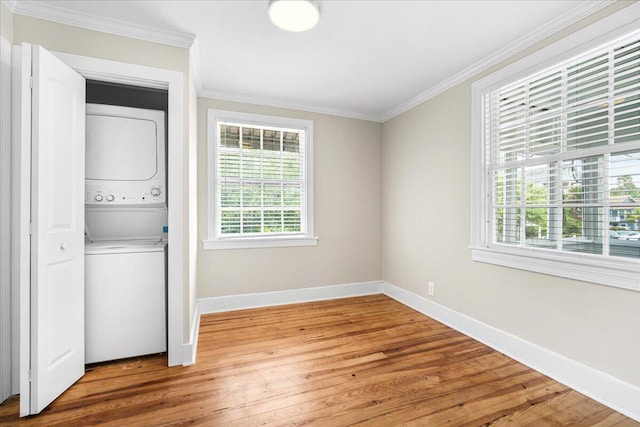 laundry room with estacked washer and dryer, ornamental molding, baseboards, and wood finished floors