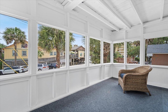sunroom / solarium featuring carpet, a decorative wall, plenty of natural light, and beamed ceiling