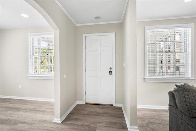 foyer entrance featuring arched walkways, wood finished floors, crown molding, and baseboards