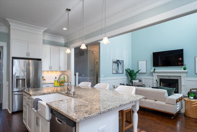 kitchen featuring white cabinetry, a kitchen breakfast bar, hanging light fixtures, appliances with stainless steel finishes, and an island with sink