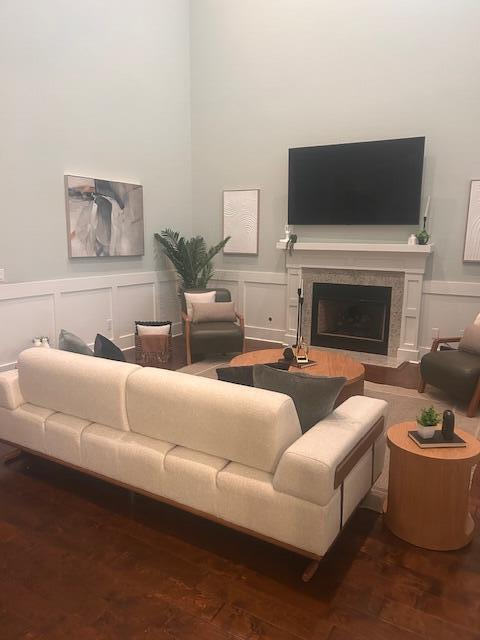 living room featuring a fireplace with flush hearth, wainscoting, a decorative wall, and wood finished floors