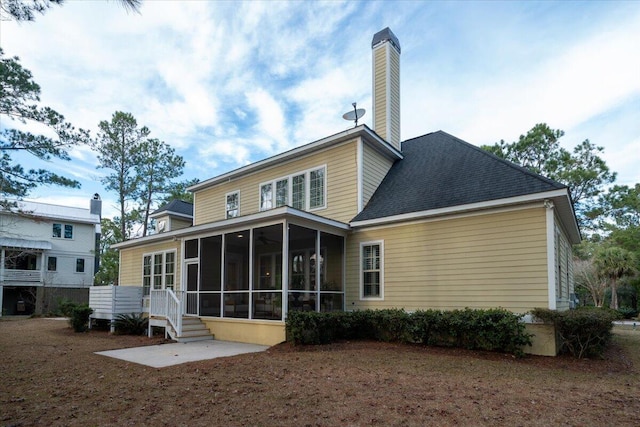 back of house with a shingled roof, a sunroom, a patio area, and a chimney