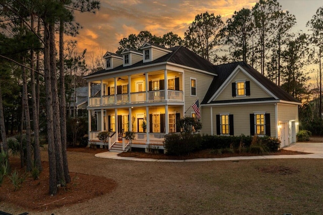 back of house at dusk featuring a balcony, covered porch, driveway, and a garage