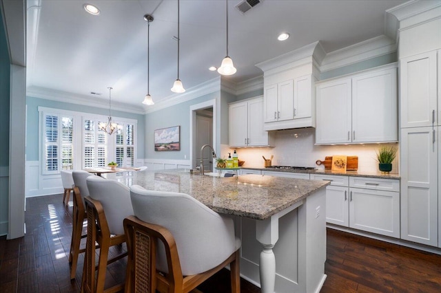 kitchen featuring a sink, visible vents, white cabinetry, an island with sink, and pendant lighting