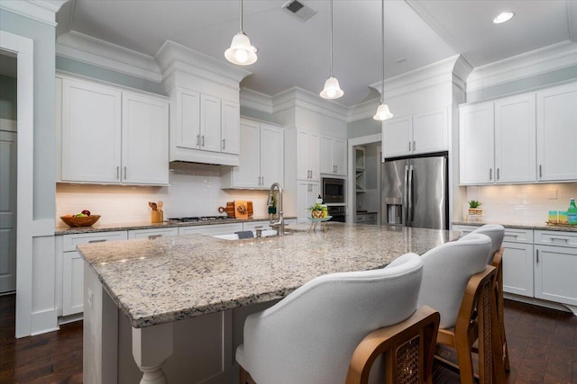 kitchen with appliances with stainless steel finishes, visible vents, a center island with sink, and decorative light fixtures