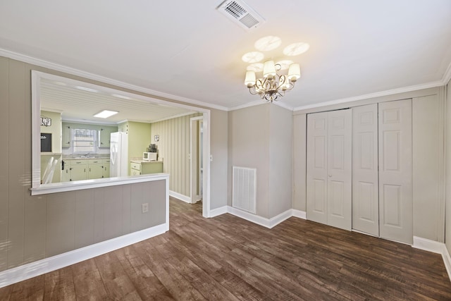 unfurnished living room with a chandelier, dark wood finished floors, ornamental molding, and baseboards