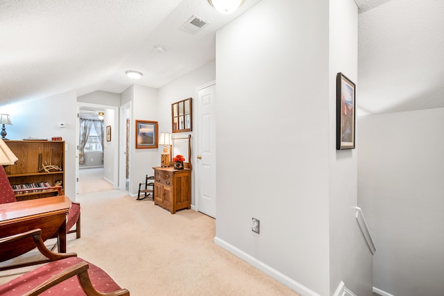 hall with a textured ceiling, lofted ceiling, and light carpet