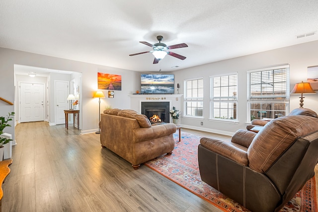 living room featuring ceiling fan, light wood-type flooring, and a textured ceiling