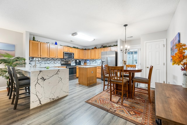 kitchen with decorative backsplash, stainless steel appliances, hanging light fixtures, and light hardwood / wood-style floors