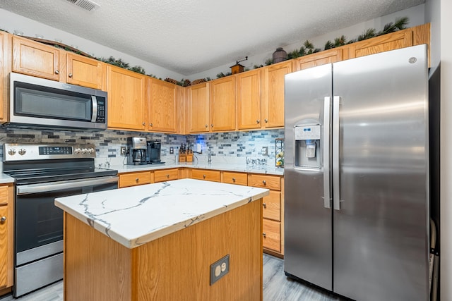 kitchen with a textured ceiling, a center island, stainless steel appliances, and tasteful backsplash