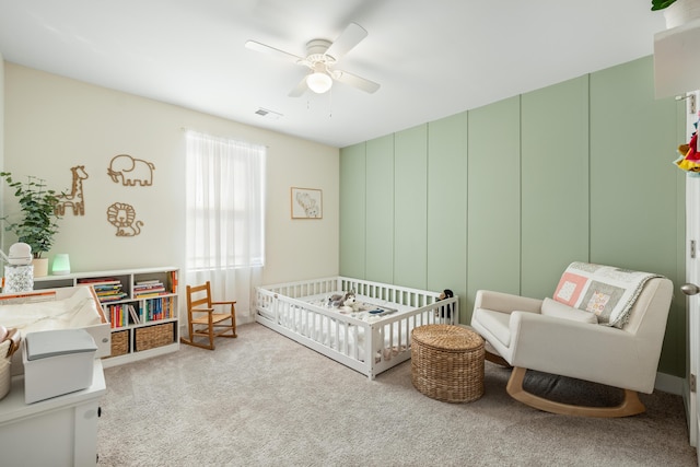 bedroom featuring ceiling fan, light colored carpet, and a crib