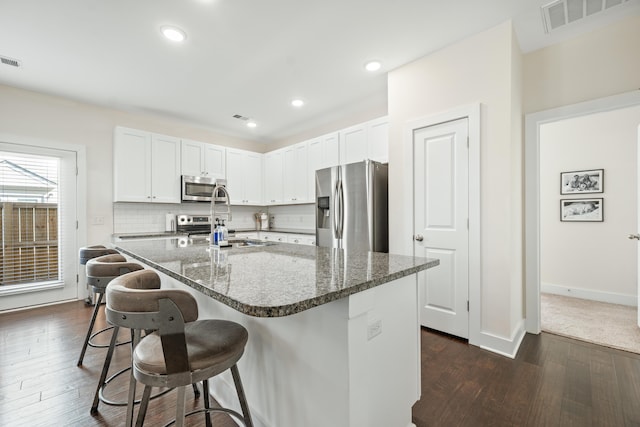 kitchen with white cabinetry, a kitchen bar, appliances with stainless steel finishes, tasteful backsplash, and dark stone countertops