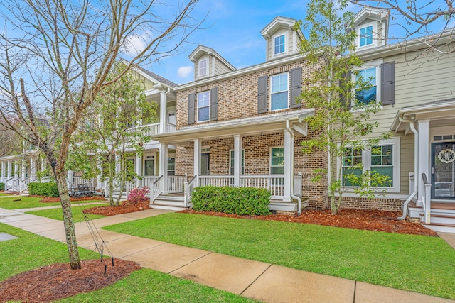 view of front of house featuring brick siding, covered porch, and a front yard