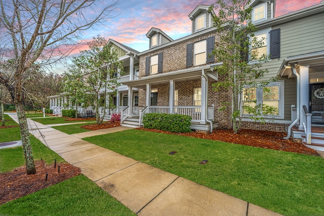 view of front of home with brick siding, a porch, and a front lawn