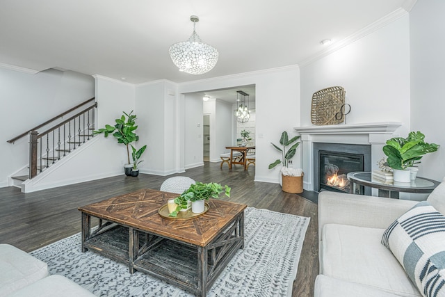 living area featuring a notable chandelier, wood finished floors, a glass covered fireplace, crown molding, and stairs