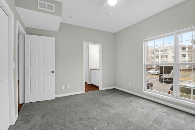 unfurnished bedroom featuring ceiling fan, ensuite bathroom, and dark colored carpet