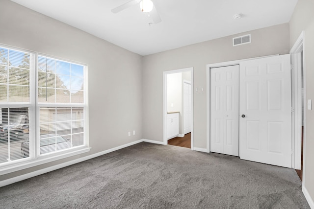 unfurnished bedroom featuring ensuite bath, a closet, ceiling fan, and dark colored carpet