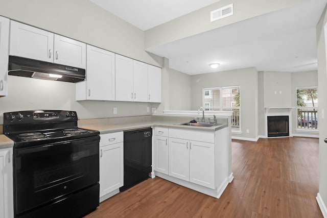 kitchen with sink, white cabinetry, wood-type flooring, black appliances, and kitchen peninsula