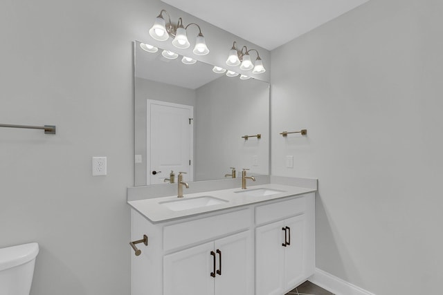 bathroom with double vanity, a sink, toilet, and baseboards